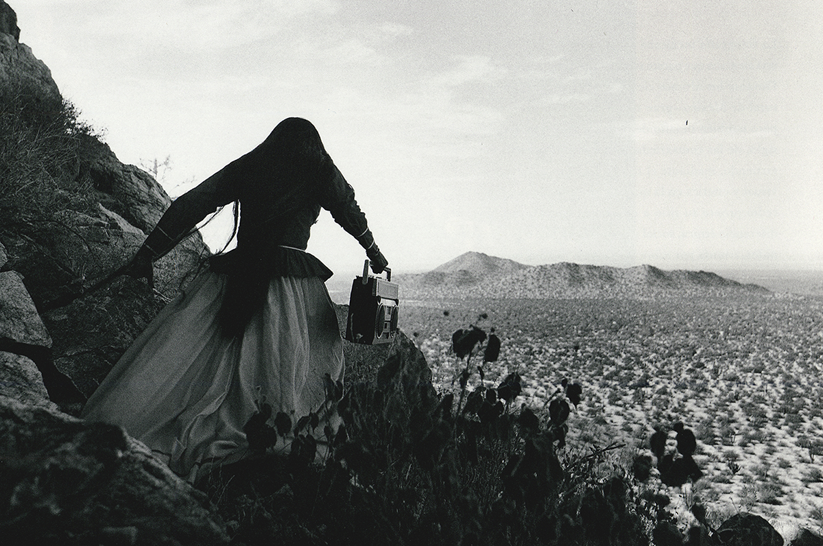 Foto en blanco y negro donde a la derecha hay una mujer de espaldas y en el fondo se ve paisaje natural