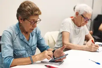 Una mujer consulta su móvil en una sesión del taller, mientras otra toma apuntes con un bolígrafo