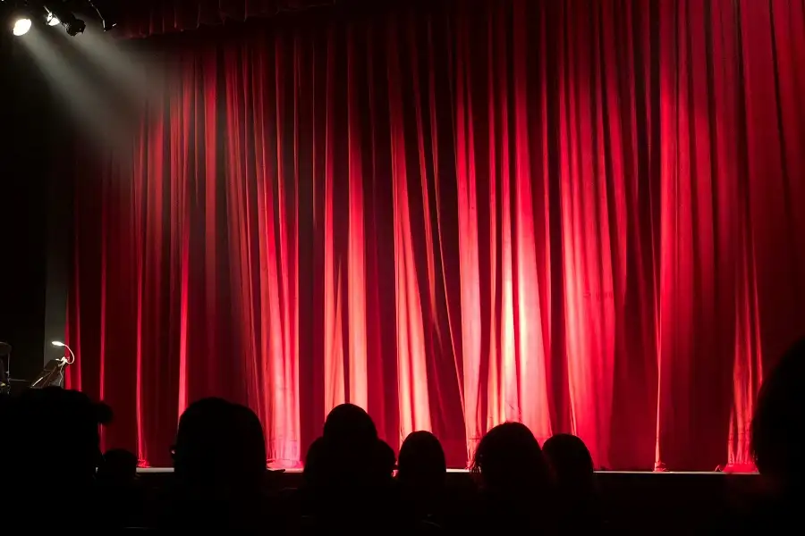 gente esperando  en un teatro con las cortinas rojas cerradas