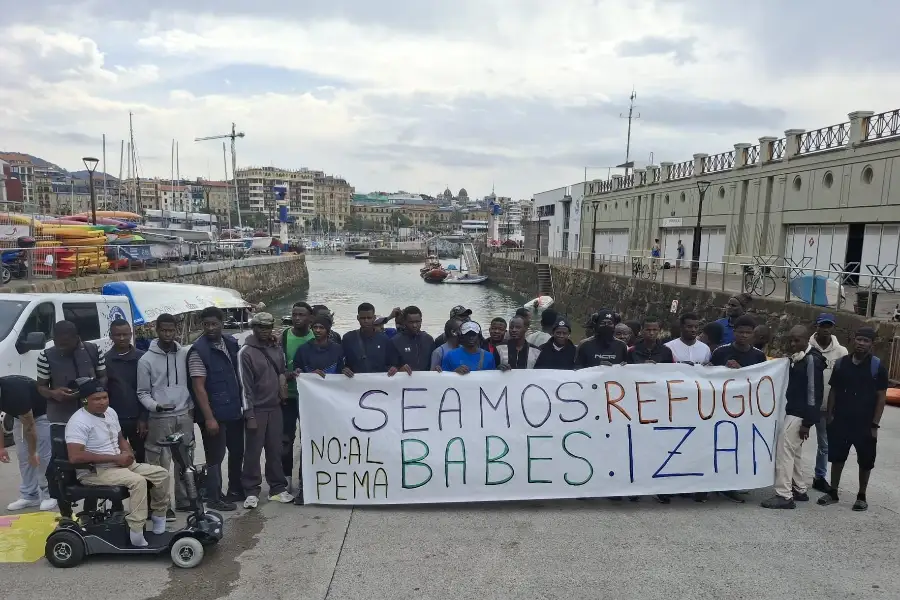 Un grupo de migrantes detrás de una pancarta en el muelle donostiarra