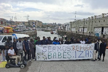 Un grupo de migrantes detrás de una pancarta en el muelle donostiarra