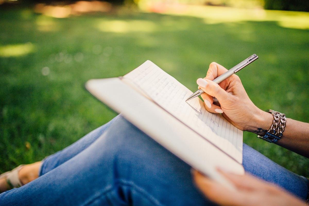 Persona sentada en un jardín tomando notas en un cuaderno.